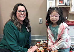 Woman in green shirt and glasses. Child in blue dress and pink and white jacket and glasses.